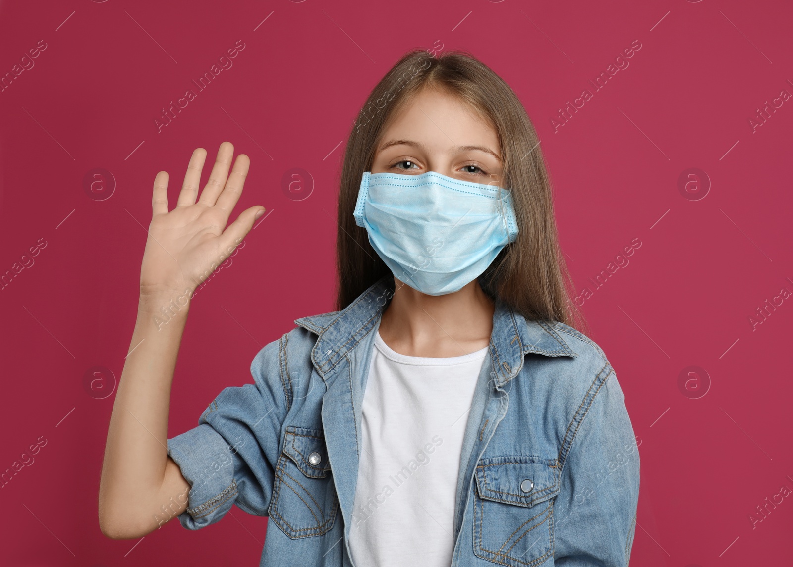 Photo of Little girl in protective mask showing hello gesture on crimson background. Keeping social distance during coronavirus pandemic