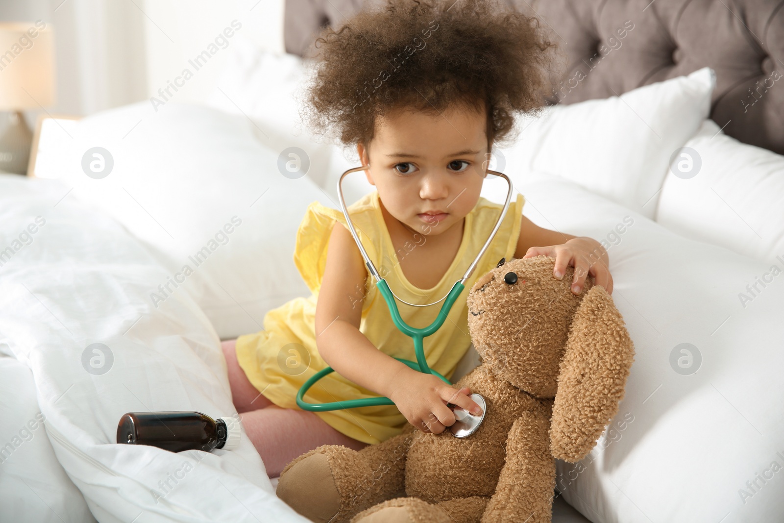 Photo of Cute African American child imagining herself as doctor while playing with stethoscope and toy bunny at home