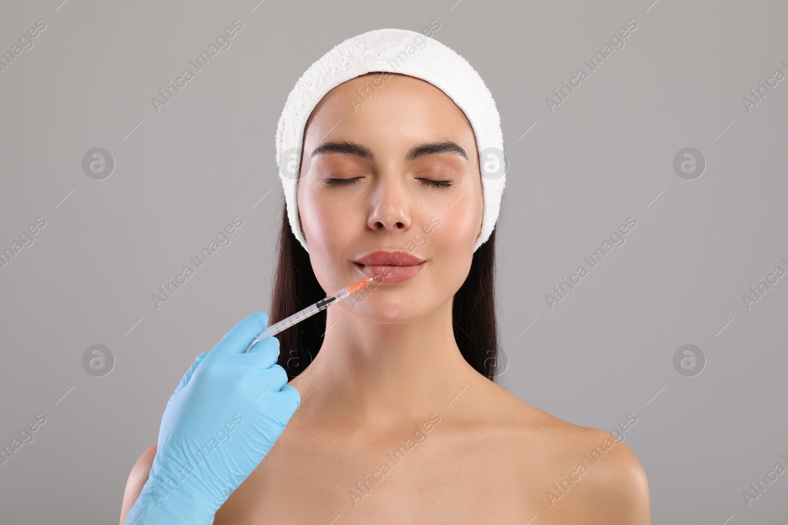 Photo of Doctor giving lips injection to young woman on light grey background. Cosmetic surgery