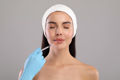 Doctor giving lips injection to young woman on light grey background. Cosmetic surgery