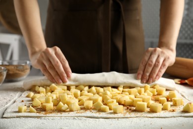 Photo of Woman making delicious apple strudel at table, closeup