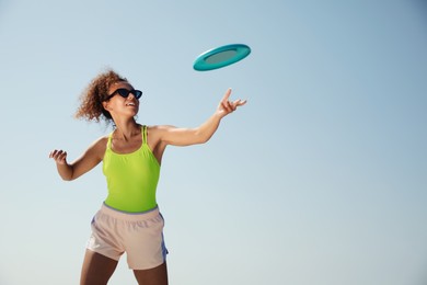 Photo of Happy African American woman throwing flying disk against blue sky on sunny day