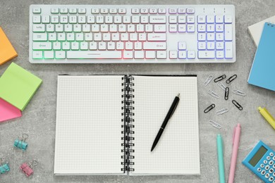 Photo of Modern keyboard with RGB lighting and stationery on grey table, flat lay