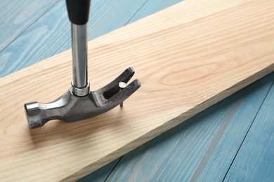Photo of Hammer pulling metal nail out of plank on light blue table, closeup