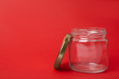 Photo of Open empty glass jar on red background, space for text