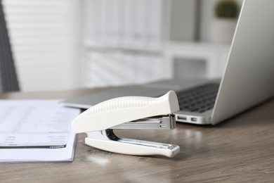 Photo of Stapler and document on wooden table indoors, closeup