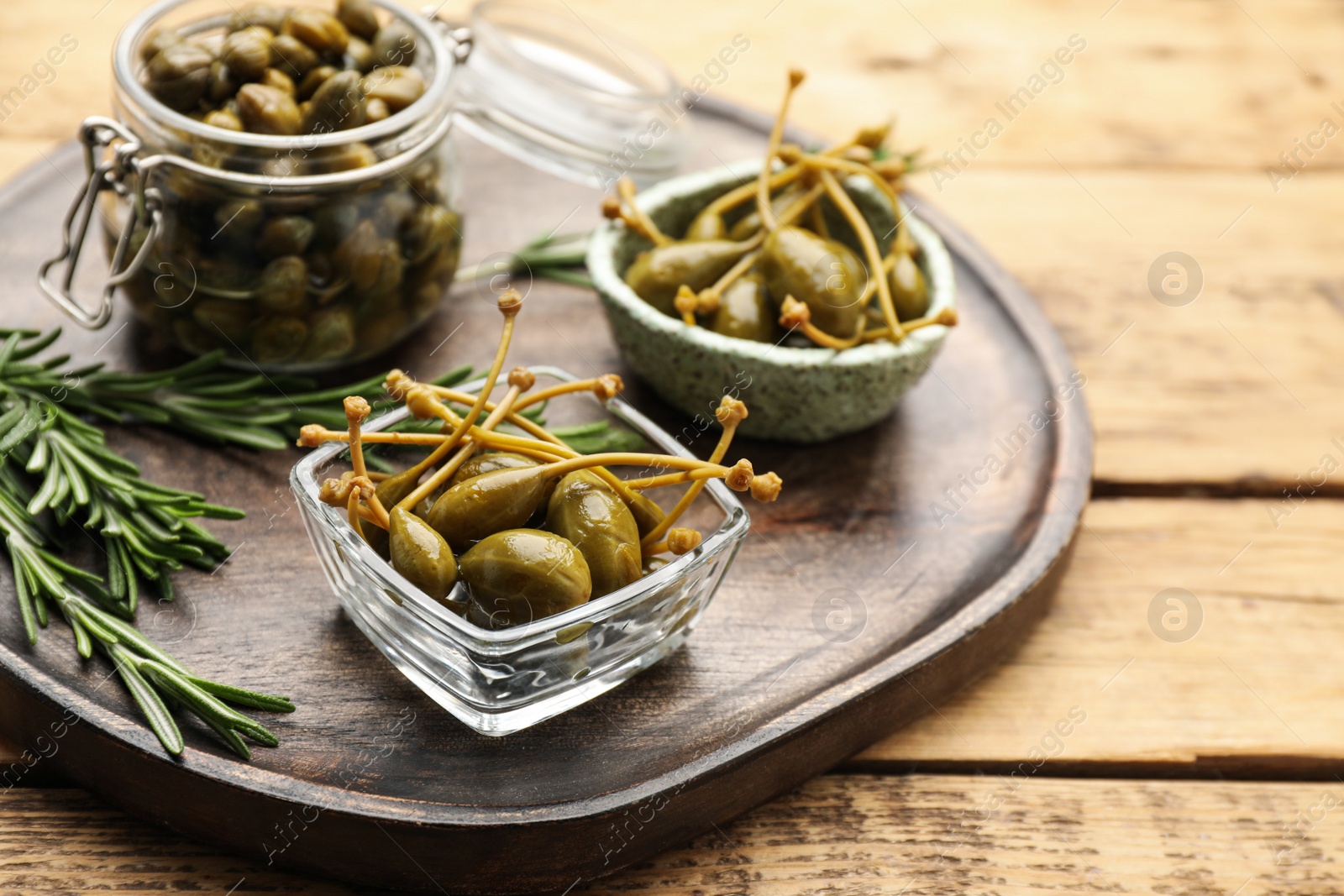 Photo of Delicious pickled capers and rosemary on wooden table