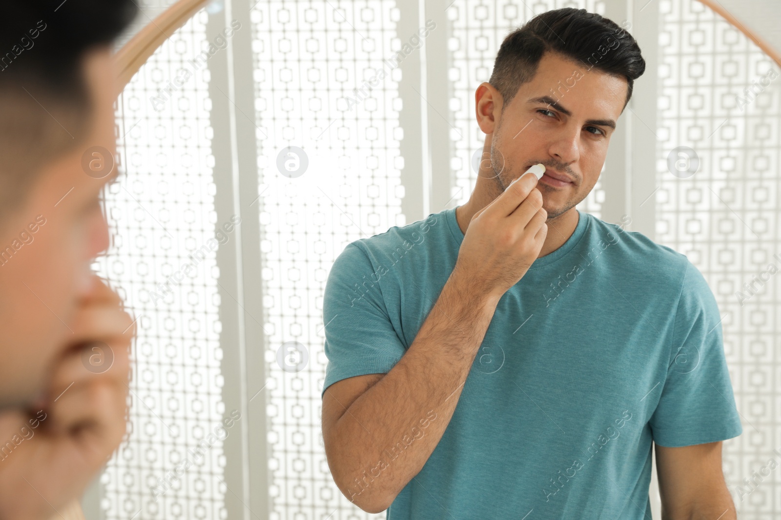 Photo of Man applying hygienic lip balm in front of mirror at home