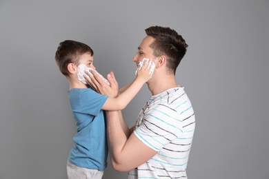 Photo of Dad and his little son applying shaving foam against color background
