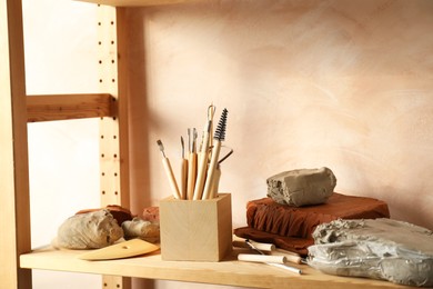 Photo of Clay and set of modeling tools on wooden rack in workshop