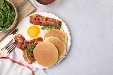 Photo of Tasty pancakes with fried egg and bacon served on light grey table, flat lay. Space for text