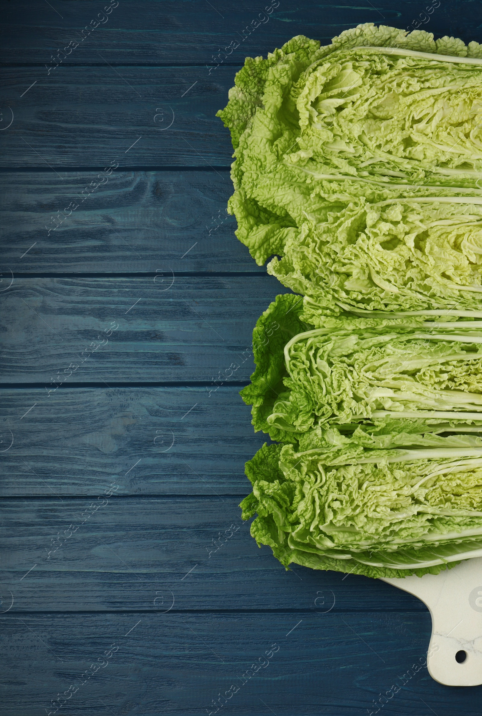 Photo of Cut fresh ripe Chinese cabbages on blue wooden table, flat lay. Space for text