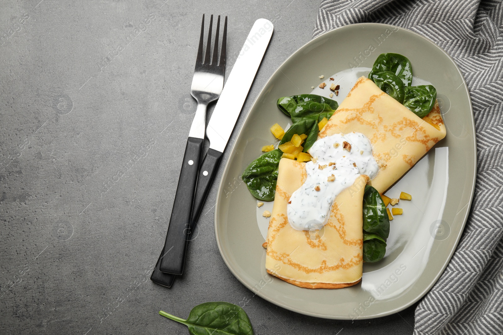 Photo of Delicious thin pancakes with spinach and sour cream on grey table, flat lay
