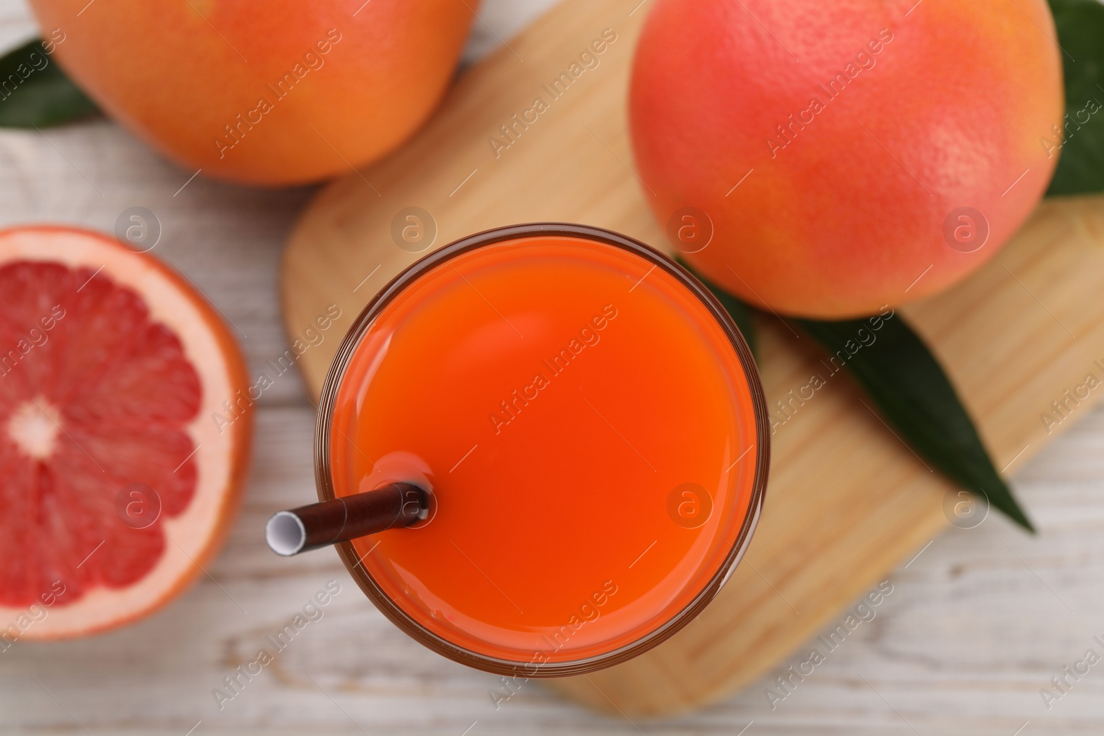 Photo of Tasty grapefruit juice in glass and fresh fruits on light wooden table, flat lay