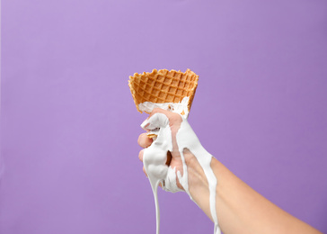 Photo of Woman holding crushed wafer cone with molten ice cream on violet background, closeup