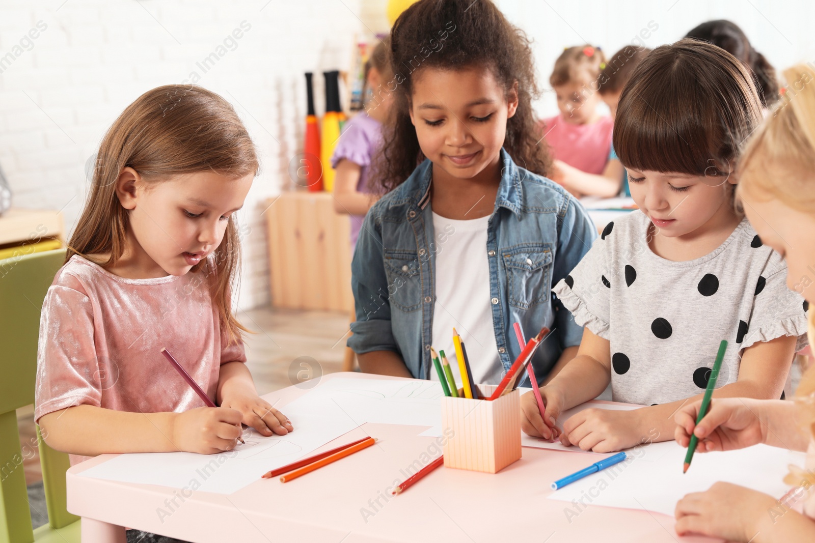 Photo of Adorable children drawing together at table indoors. Kindergarten playtime activities