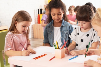 Photo of Adorable children drawing together at table indoors. Kindergarten playtime activities