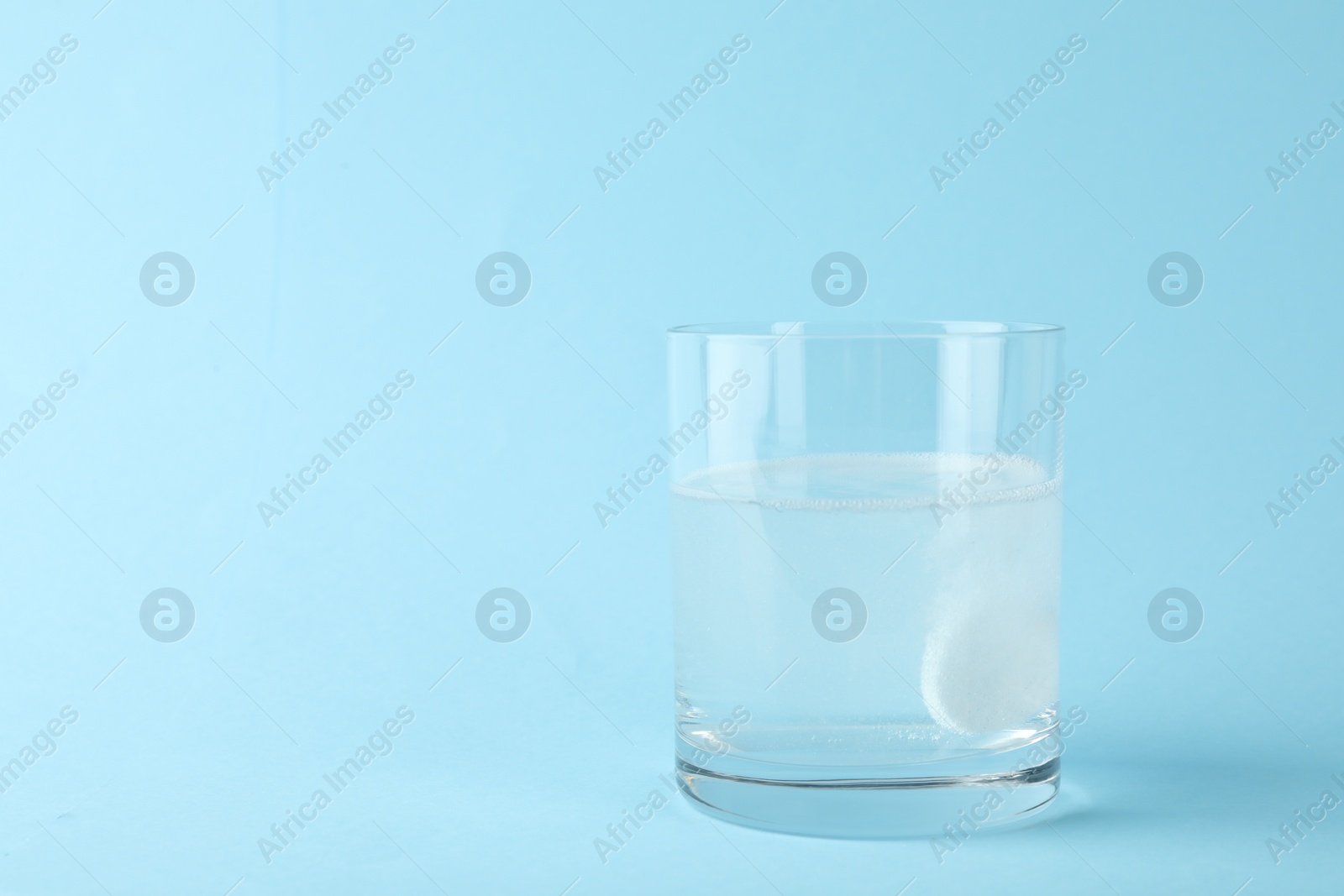 Photo of Glass of water with effervescent tablet on light blue background, space for text