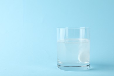 Photo of Glass of water with effervescent tablet on light blue background, space for text