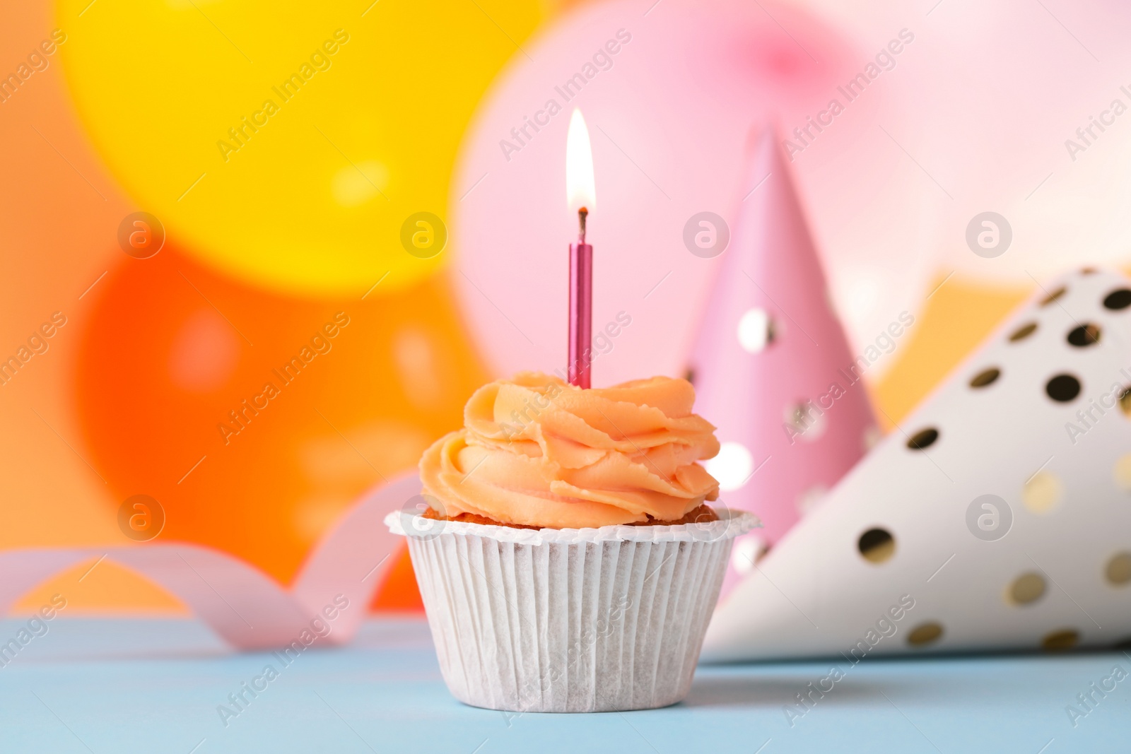 Photo of Tasty birthday cupcake with candle and party hats on light blue table