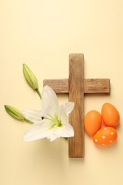 Photo of Wooden cross, painted Easter eggs and lily flowers on pale yellow background, flat lay