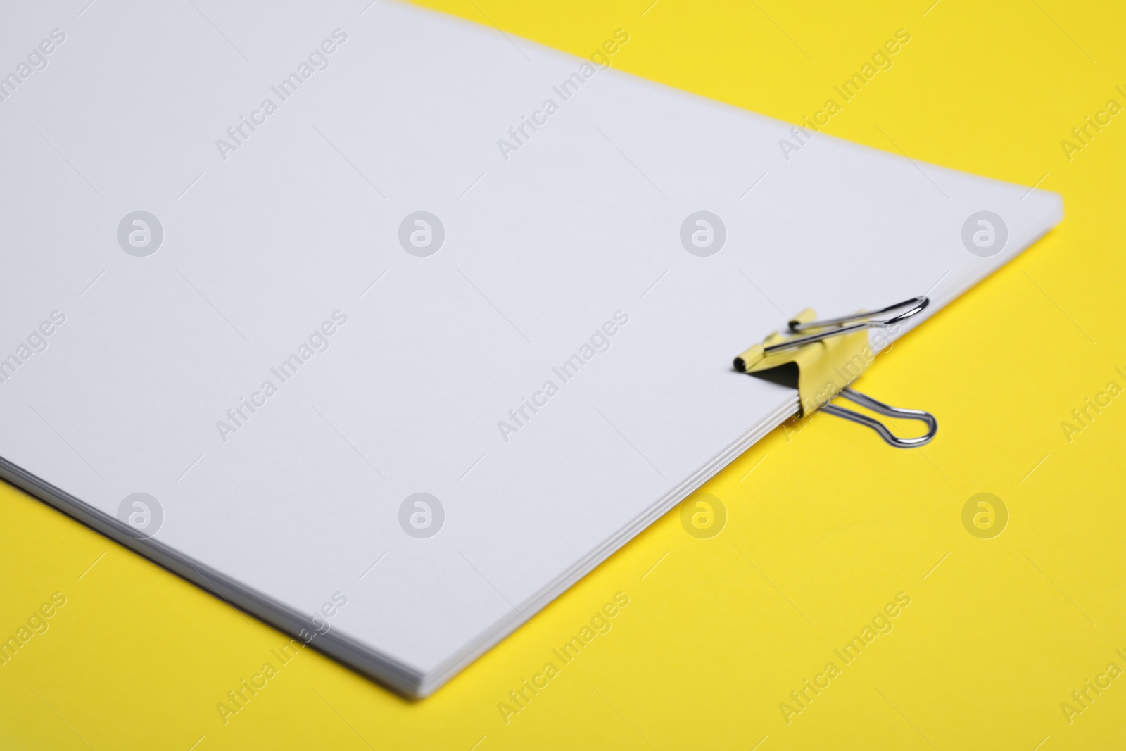 Photo of Sheets of paper with clip on yellow background, closeup