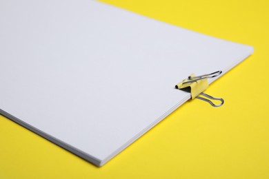 Photo of Sheets of paper with clip on yellow background, closeup