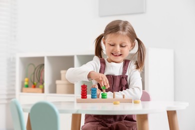 Cute little girl playing with stacking and counting game at white table indoors, space for text. Child's toy