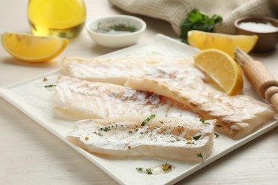 Photo of Fresh raw cod fillets with spices and lemon on white wooden table