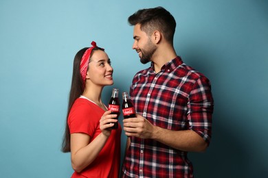 MYKOLAIV, UKRAINE - JANUARY 27, 2021: Young couple holding bottles of Coca-Cola on light blue background