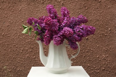 Photo of Beautiful lilac flowers in teapot near brown wall