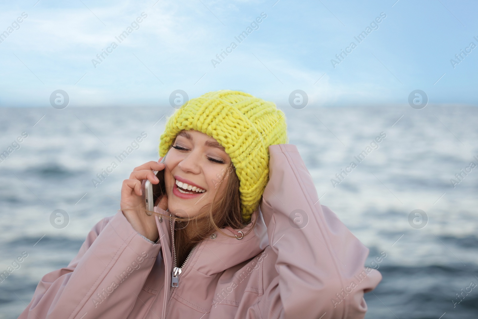 Photo of Young woman talking on mobile phone near sea