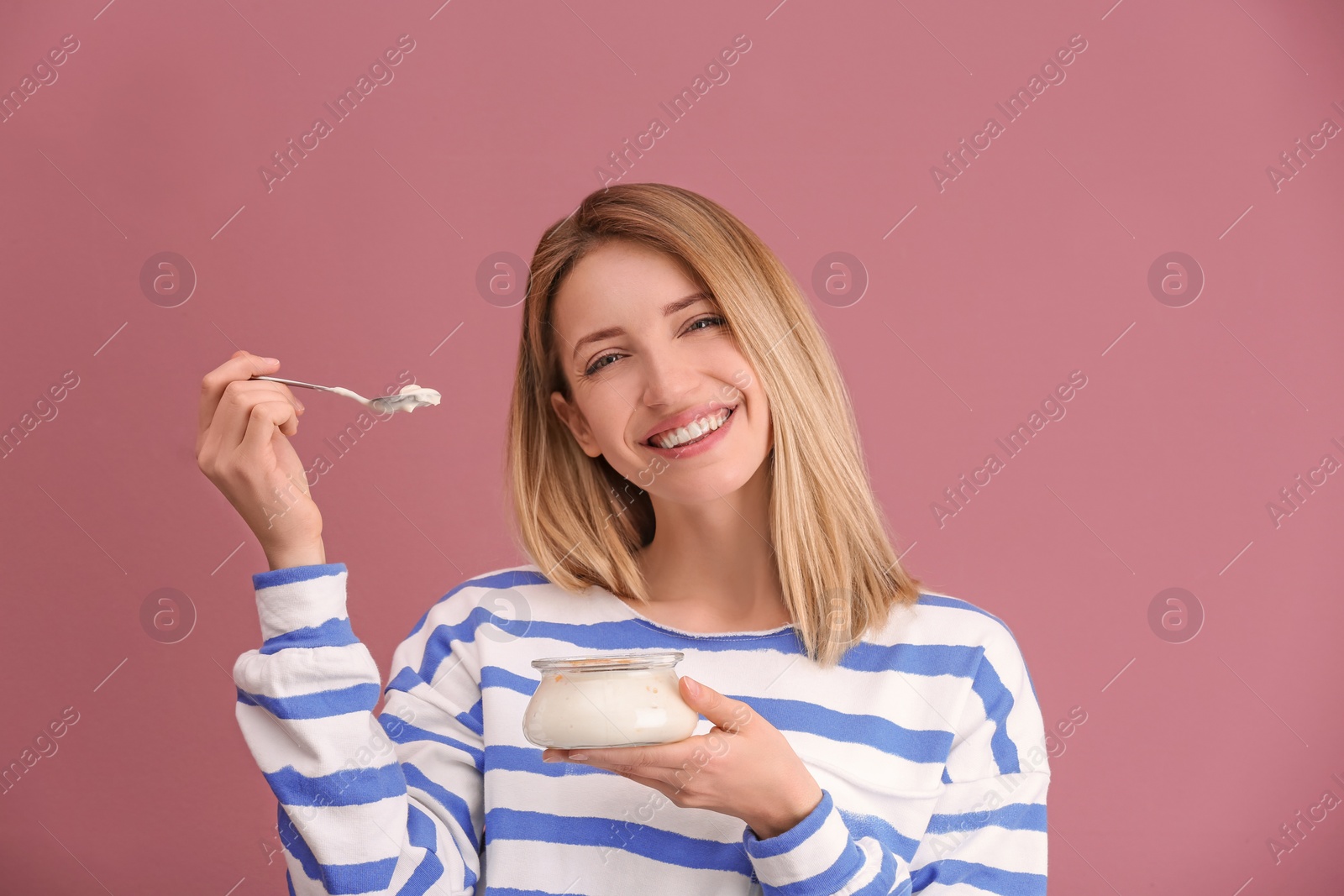 Photo of Young attractive woman eating tasty yogurt on color background