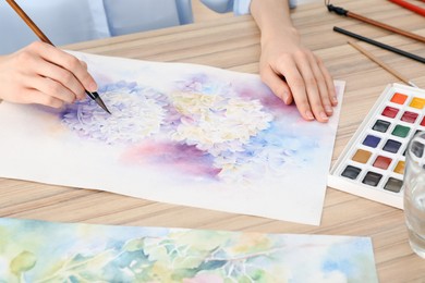 Woman painting flowers with watercolor at wooden table, closeup. Creative artwork