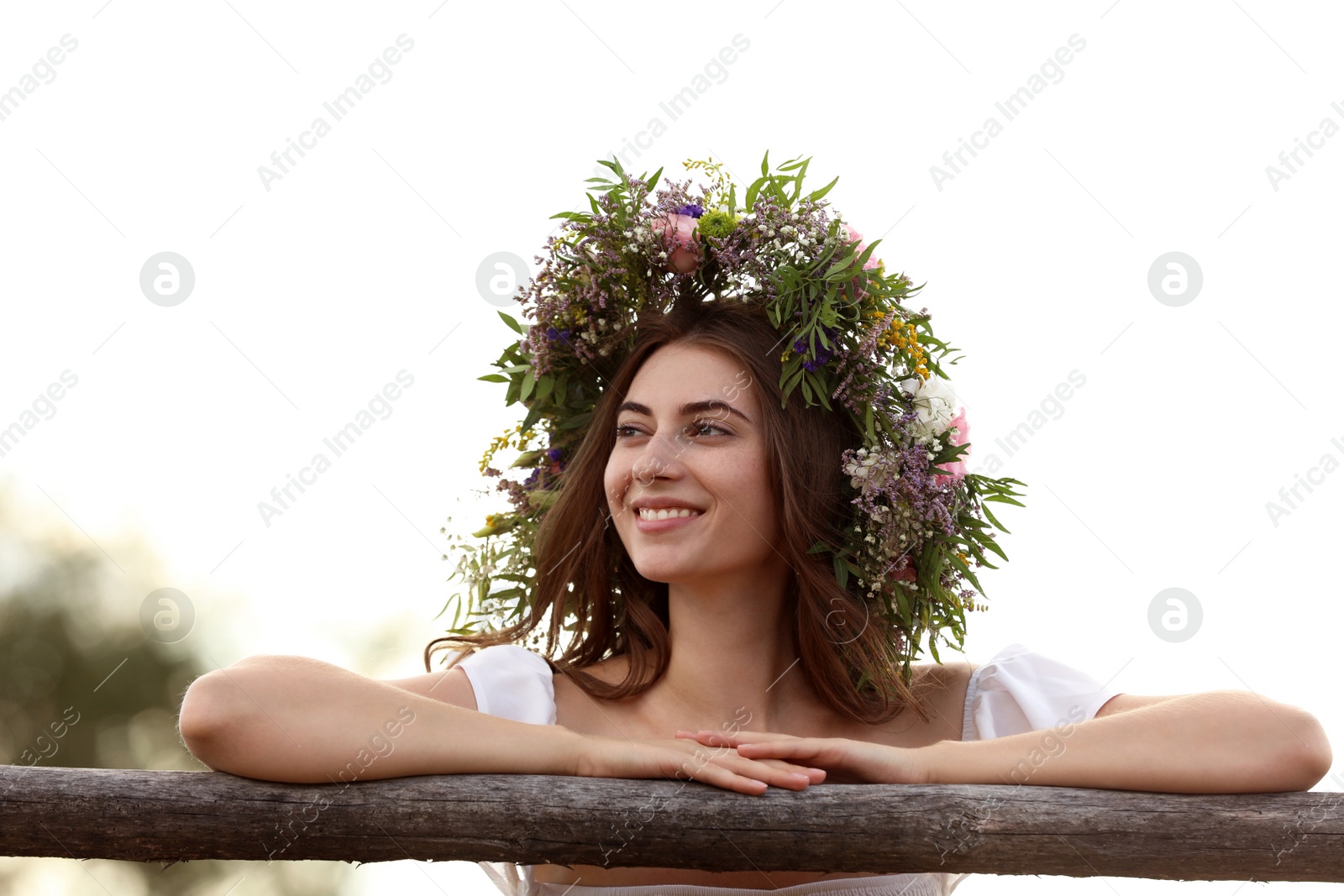 Photo of Young woman wearing wreath made of beautiful flowers near wooden fence