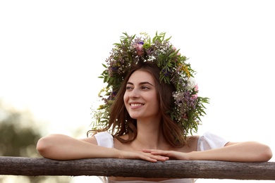 Photo of Young woman wearing wreath made of beautiful flowers near wooden fence