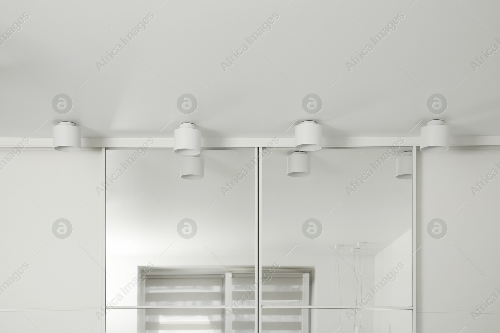 Photo of Stylish lamps near mirror on white ceiling