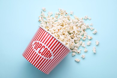 Overturned paper bucket with delicious popcorn on light blue background, flat lay