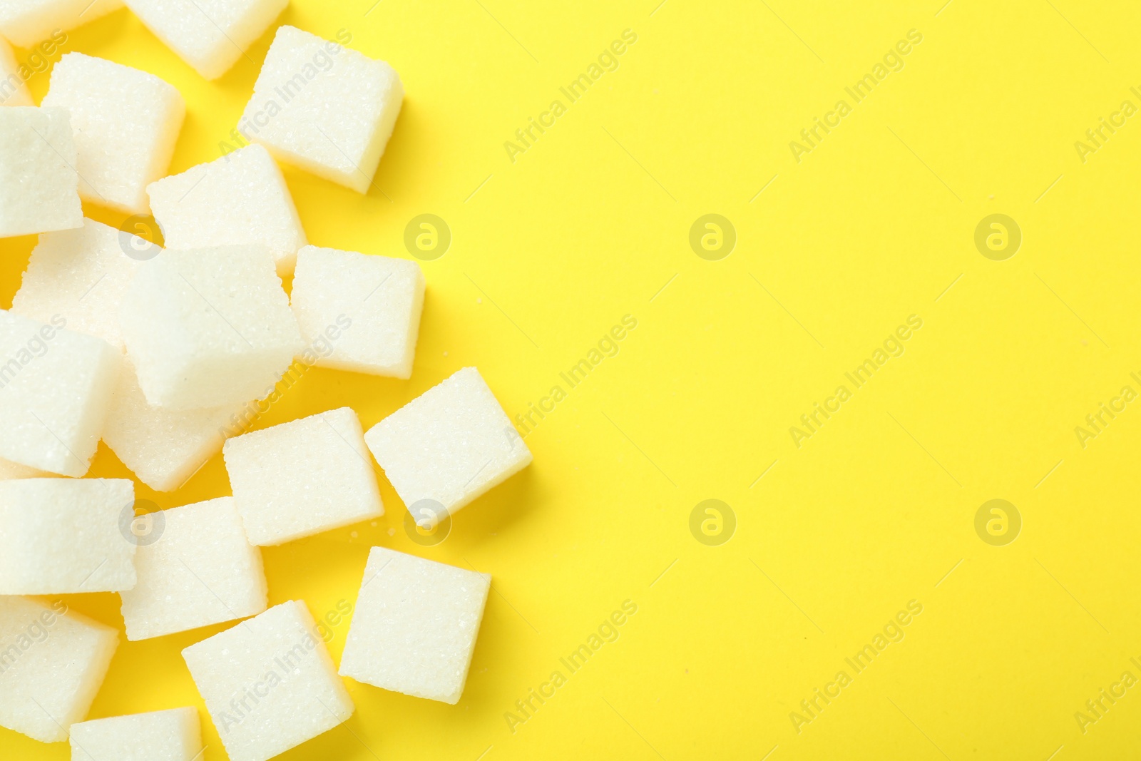 Photo of White sugar cubes on yellow background, top view. Space for text