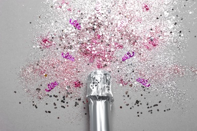 Photo of Bottle of champagne for celebration with glitter and confetti on grey background, top view