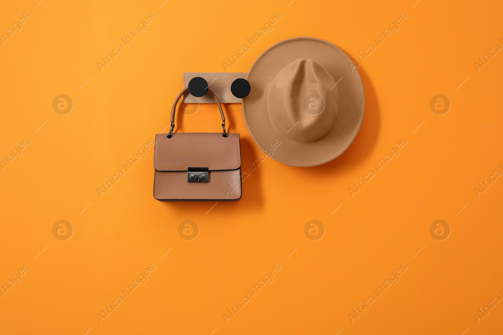 Photo of Rack with brown hat and bag on orange wall, space for text