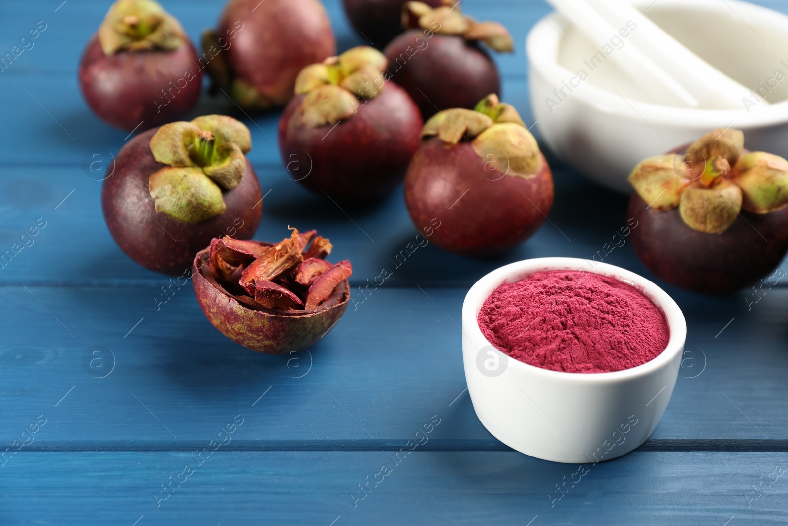 Photo of Purple mangosteen powder and fruits on blue wooden table