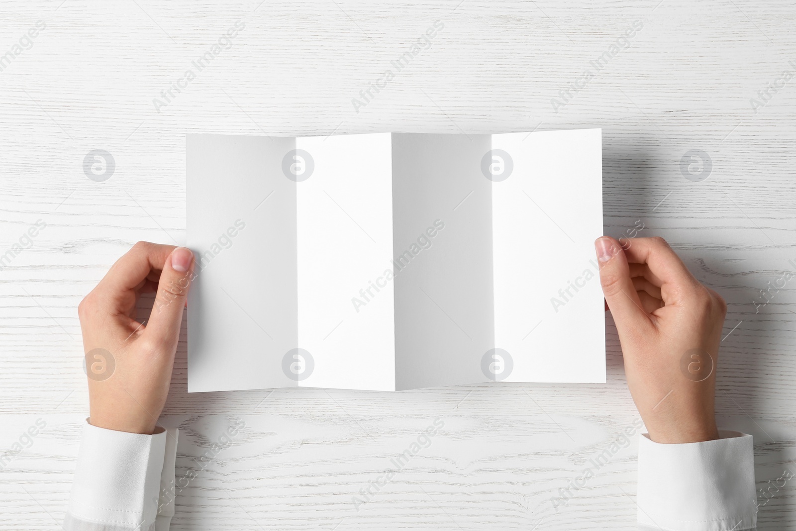 Photo of Woman holding blank brochure mock up on light background, top view