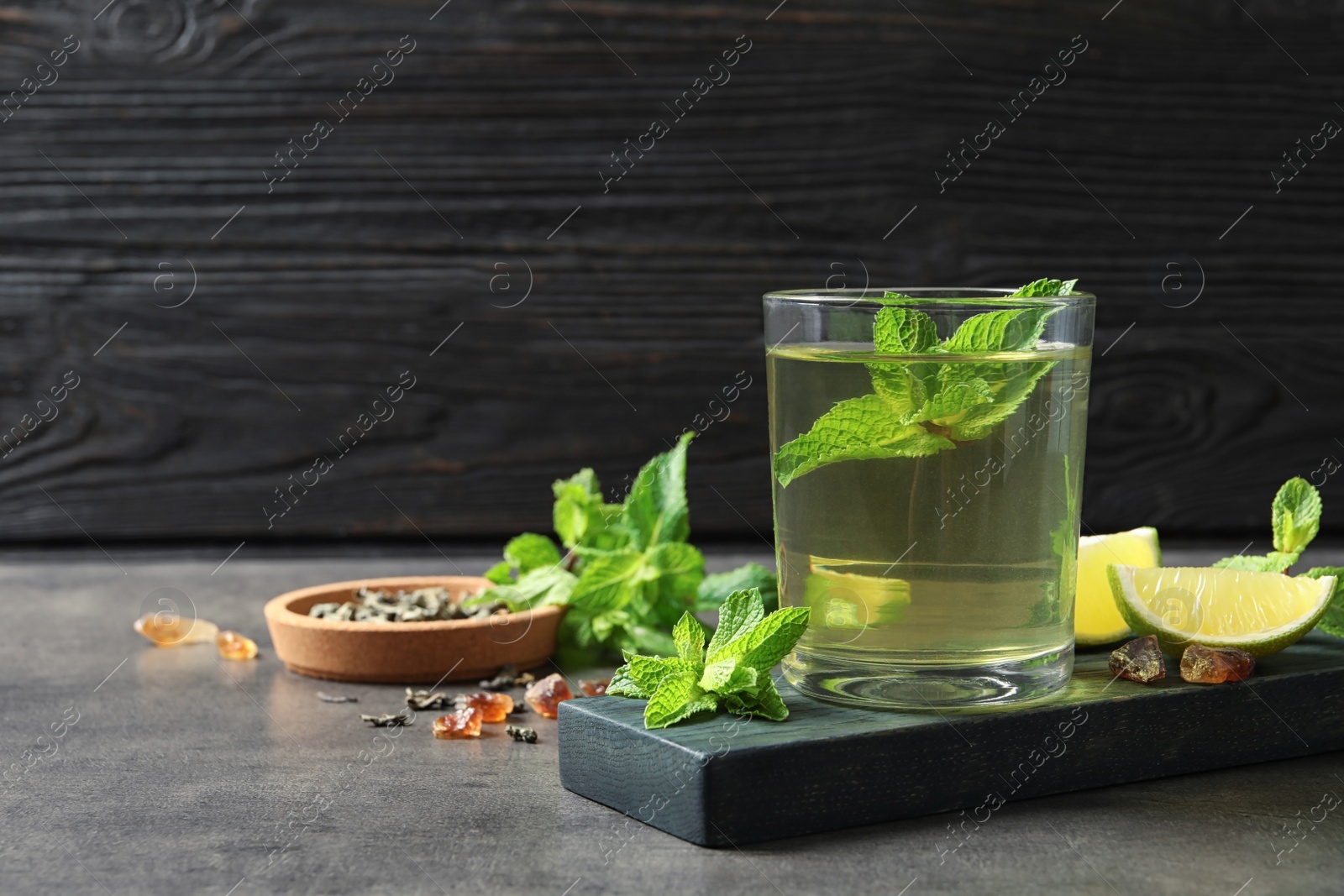 Photo of Glass with hot aromatic mint tea, fresh leaves and lime on table