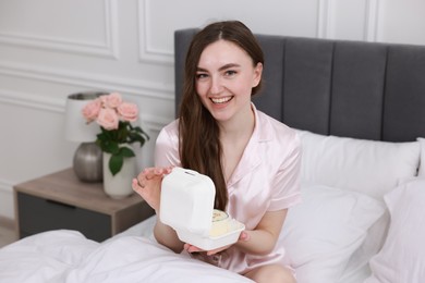 Photo of Beautiful young woman holding her Birthday cake on bed in room