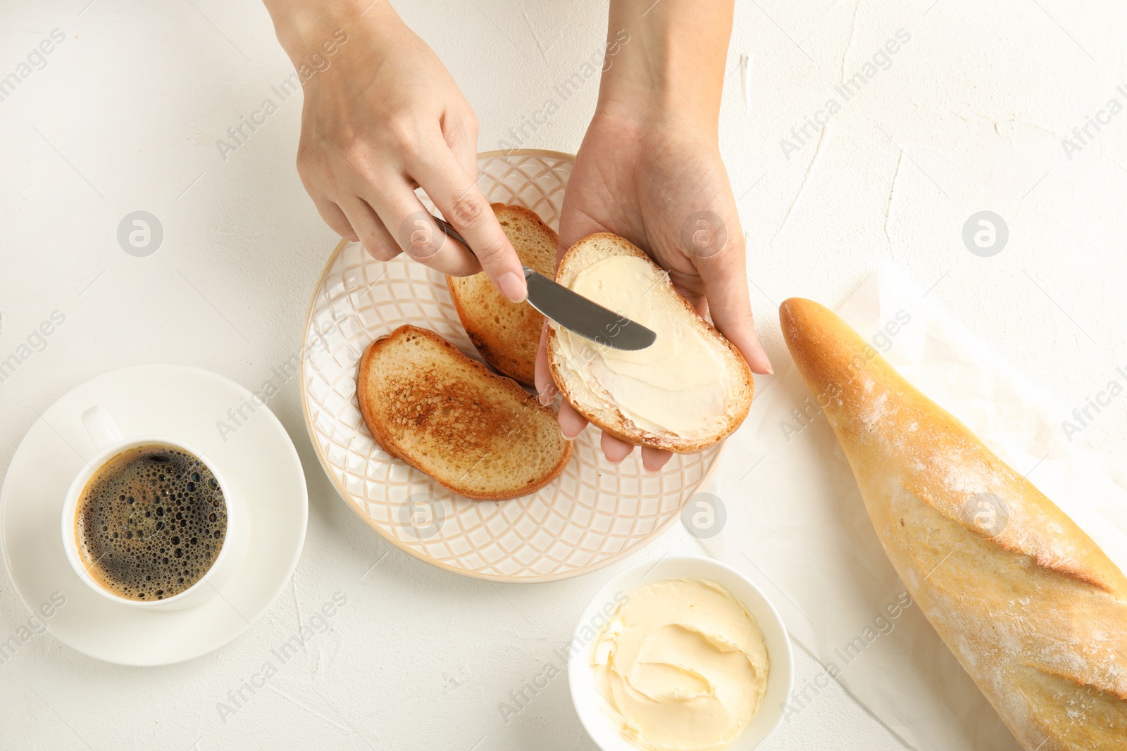 Photo of Woman spreading tasty butter onto bread over plate at white table, top view