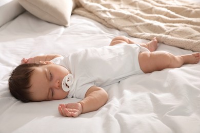 Cute little baby with pacifier sleeping on bed