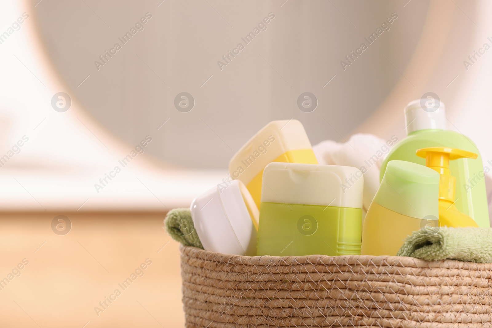 Photo of Baby cosmetic products and bath accessories in wicker basket indoors, closeup. Space for text