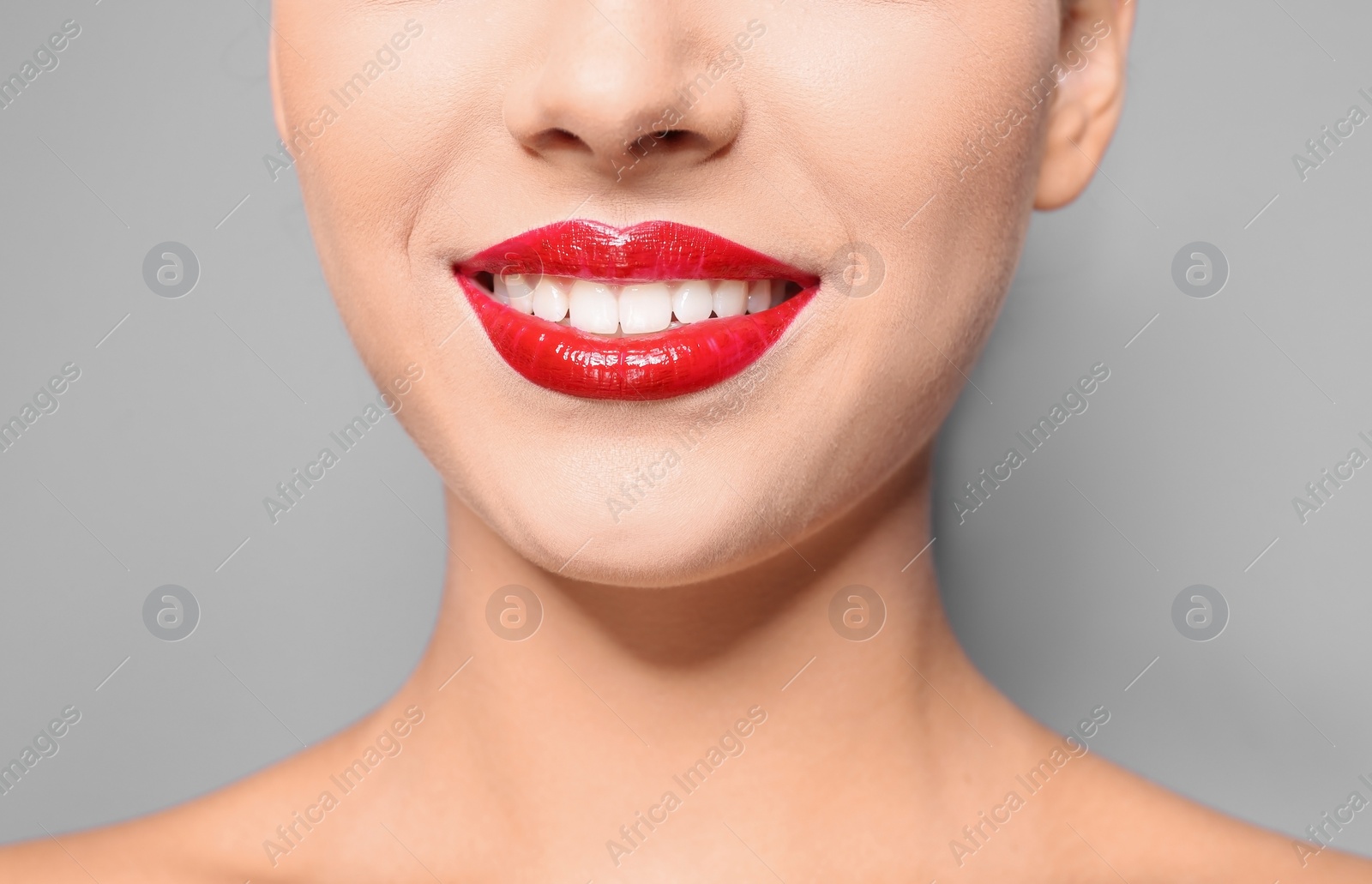 Photo of Beautiful young woman with red glossy lips on gray background, closeup