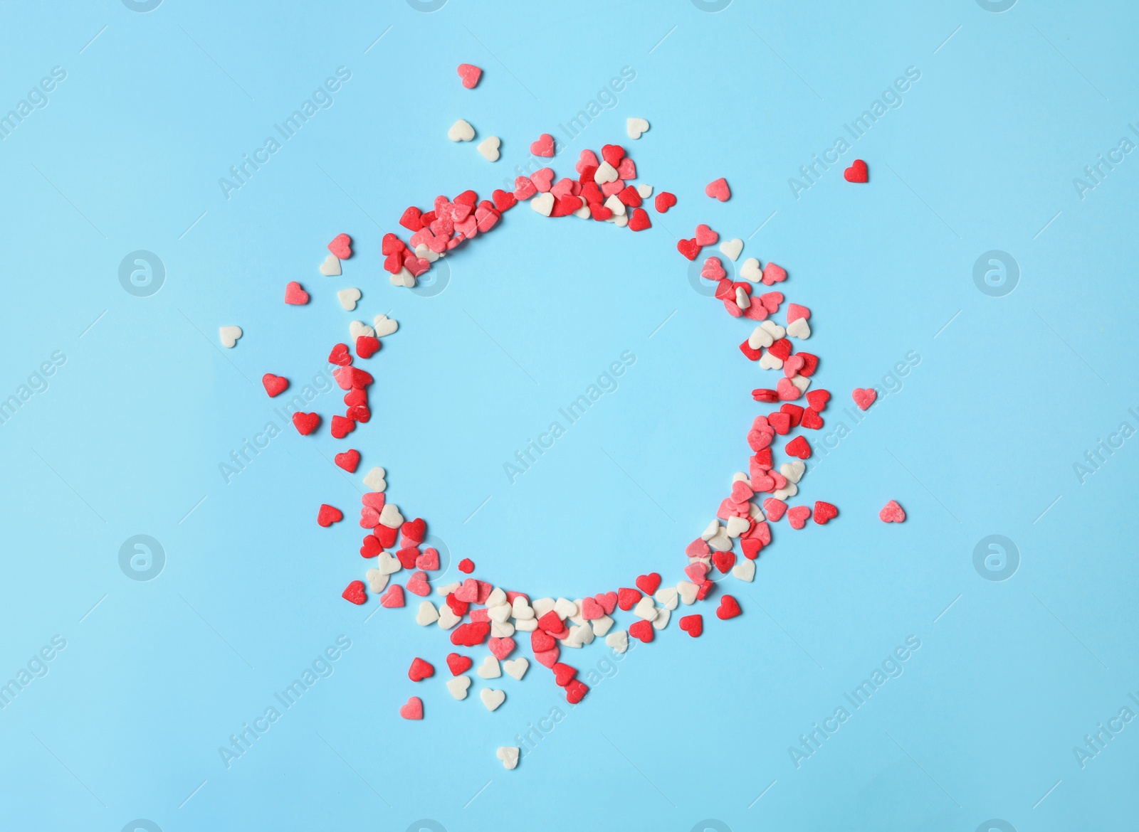 Photo of Round frame made of bright heart shaped sprinkles on light blue background, flat lay. Space for text